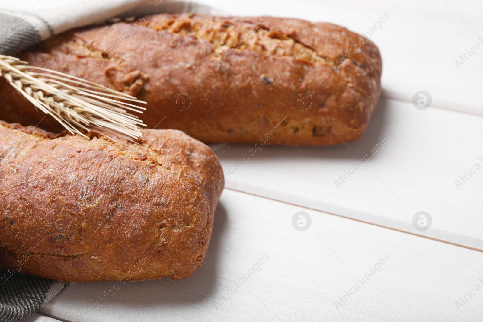 Photo of Tasty rye baguettes and spikelet on white wooden table, closeup