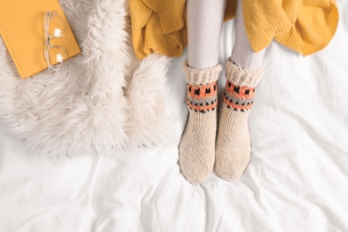 Photo of Woman wearing knitted socks on white fabric, top view. Warm clothes