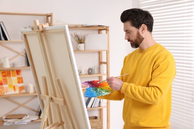 Photo of Man painting in studio. Using easel to hold canvas