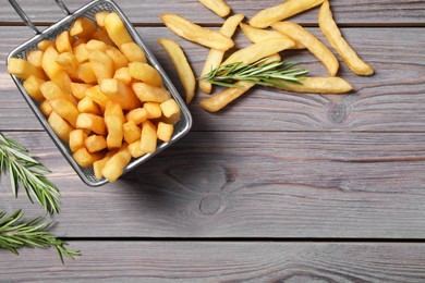 Metal basket with tasty French fries and rosemary on grey wooden table, flat lay. Space for text