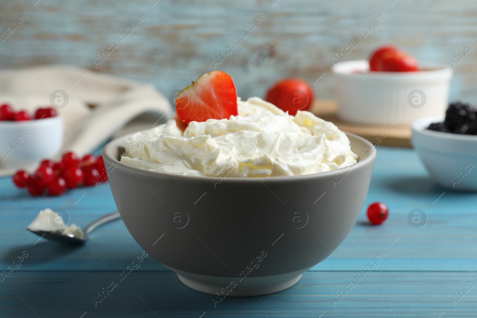 Photo of Tasty cream cheese and fresh berries on light blue wooden table
