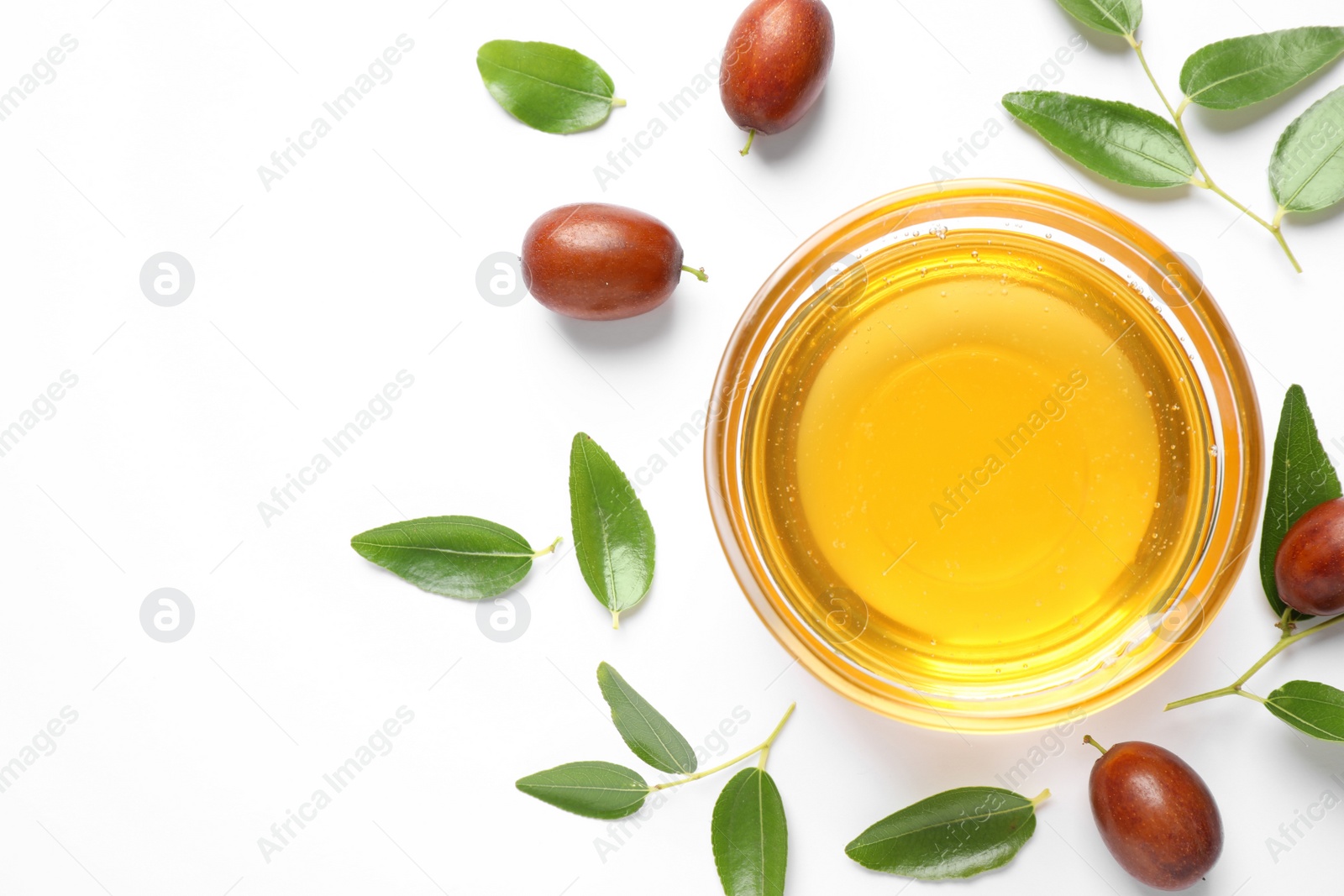 Photo of Glass bowl with jojoba oil and seeds on white background, top view