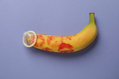 Photo of Banana with condom and red lipstick marks on violet background, top view. Safe sex concept