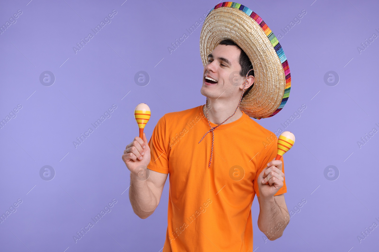 Photo of Young man in Mexican sombrero hat with maracas on violet background