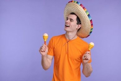 Young man in Mexican sombrero hat with maracas on violet background