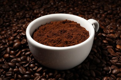 Photo of Cup with ground coffee on roasted beans, closeup