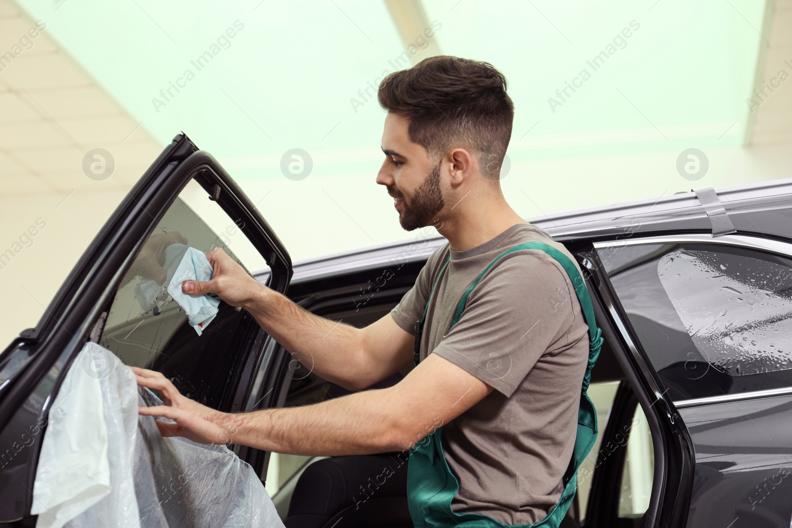 Photo of Worker washing tinted car window in workshop