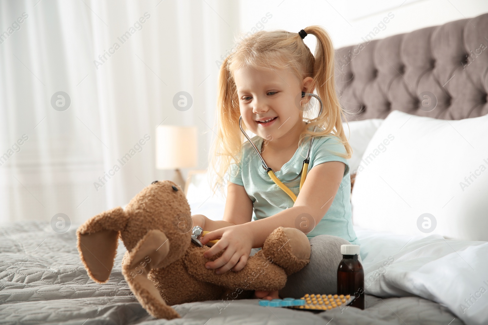 Photo of Cute child imagining herself as doctor while playing with stethoscope and toy bunny at home