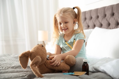 Cute child imagining herself as doctor while playing with stethoscope and toy bunny at home