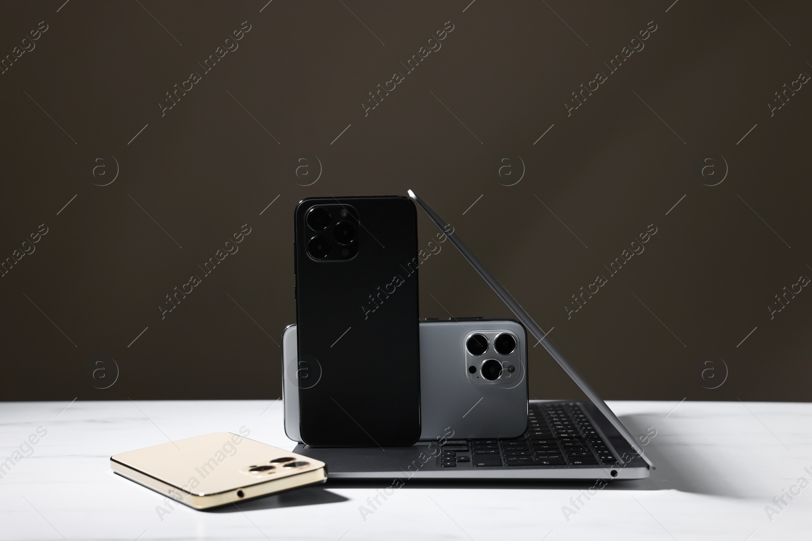 Photo of Modern laptop and smartphones on white table against brown background