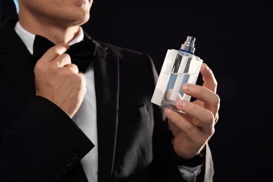 Photo of Young man with perfume bottle on black background, closeup