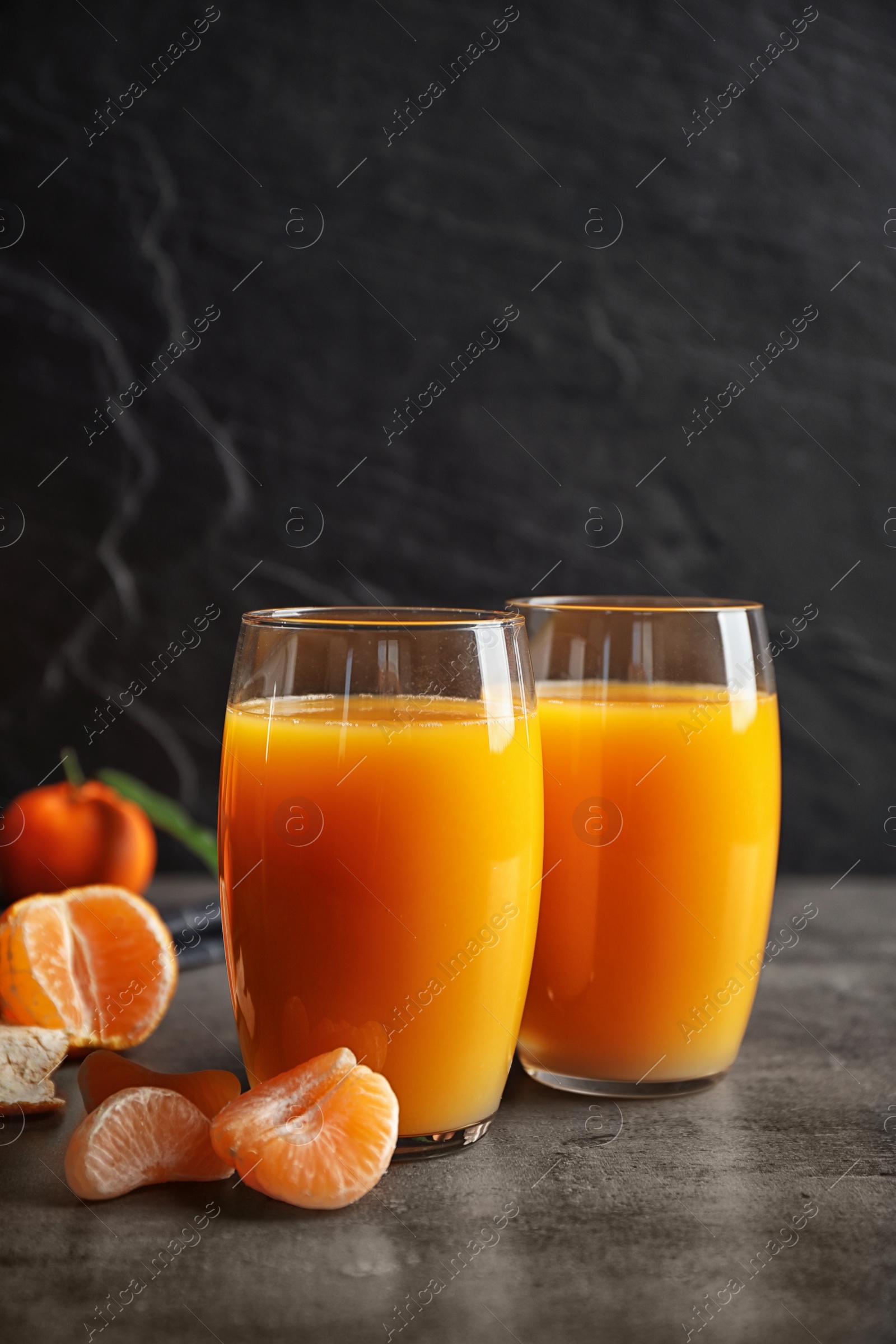 Photo of Fresh tangerines and glasses of juice on grey table