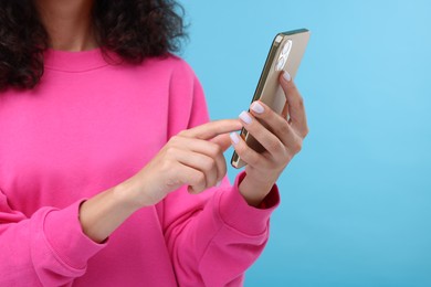 Woman sending message via smartphone on light blue background, closeup