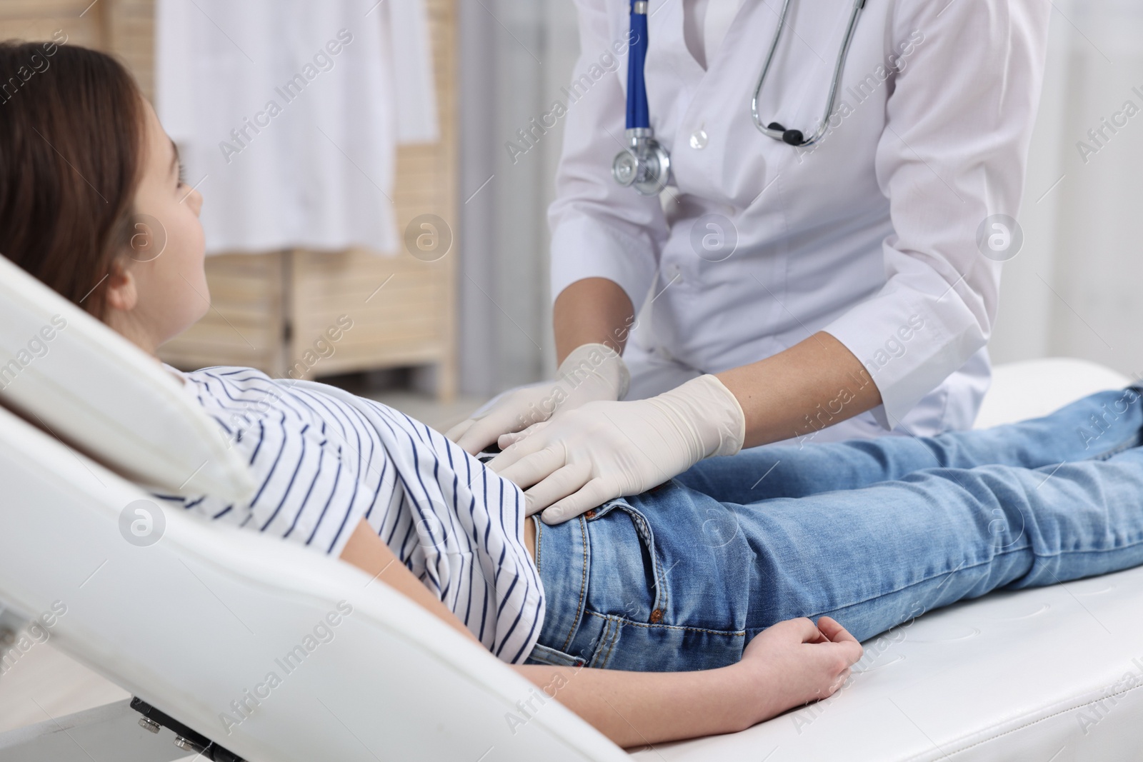 Photo of Gastroenterologist examining girl with stomach ache on couch in clinic, closeup