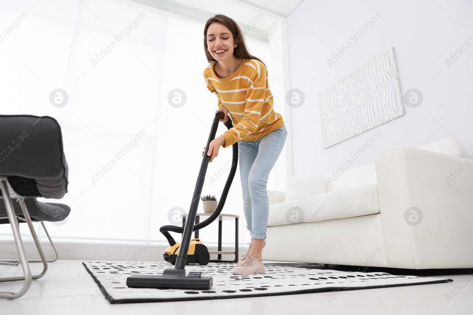 Photo of Young woman using vacuum cleaner at home