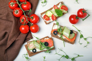 Photo of Tasty rye crispbreads with salmon, cream cheese and vegetables on white wooden table, flat lay
