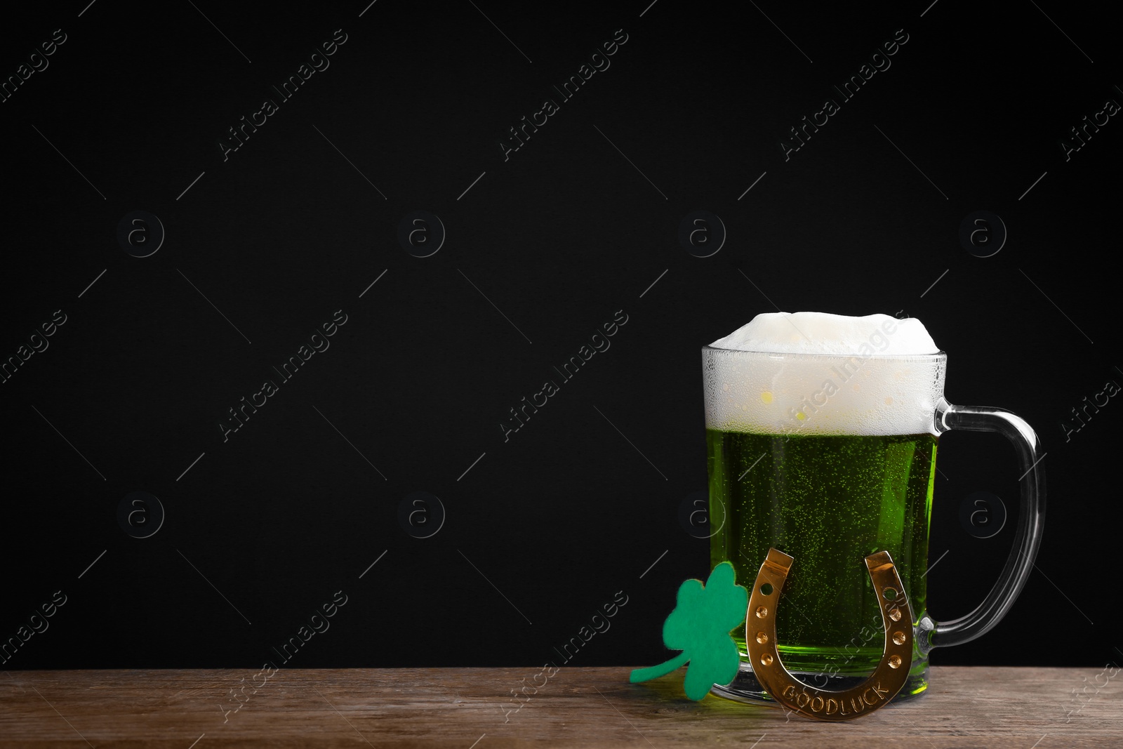 Photo of Green beer and clover on wooden table against black background, space for text. St. Patrick's Day celebration