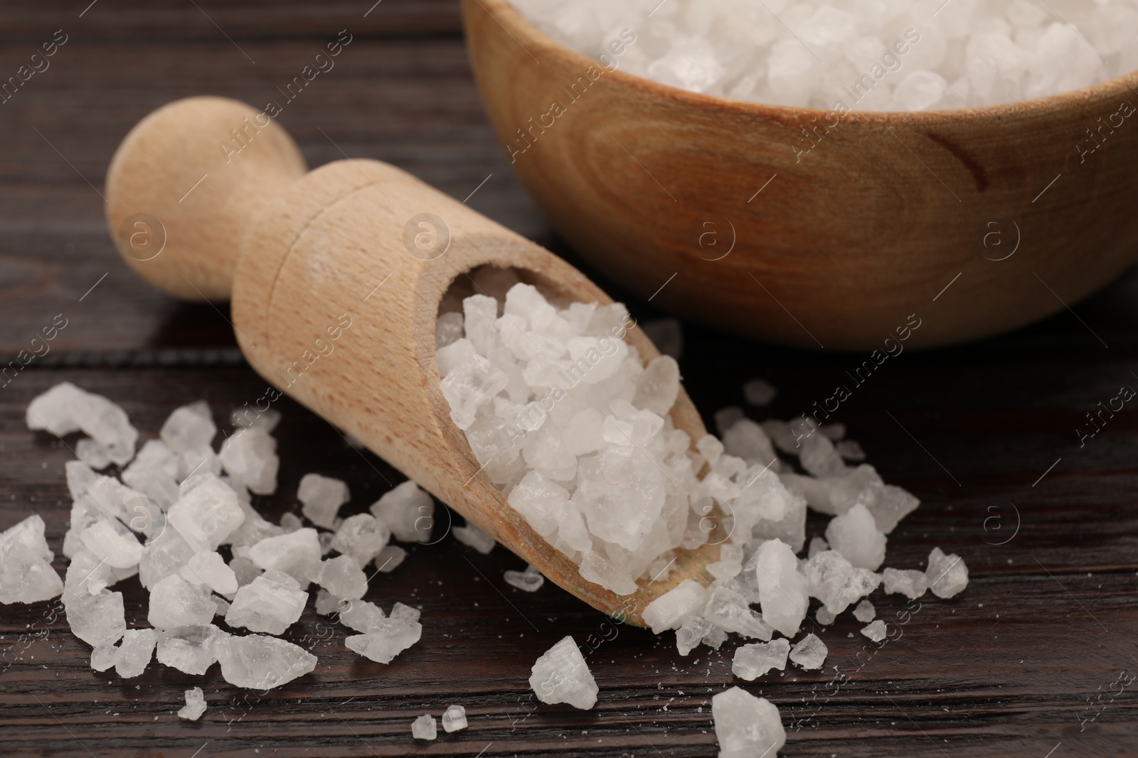 Photo of Bowl and scoop with sea salt on wooden table, closeup