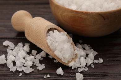 Photo of Bowl and scoop with sea salt on wooden table, closeup