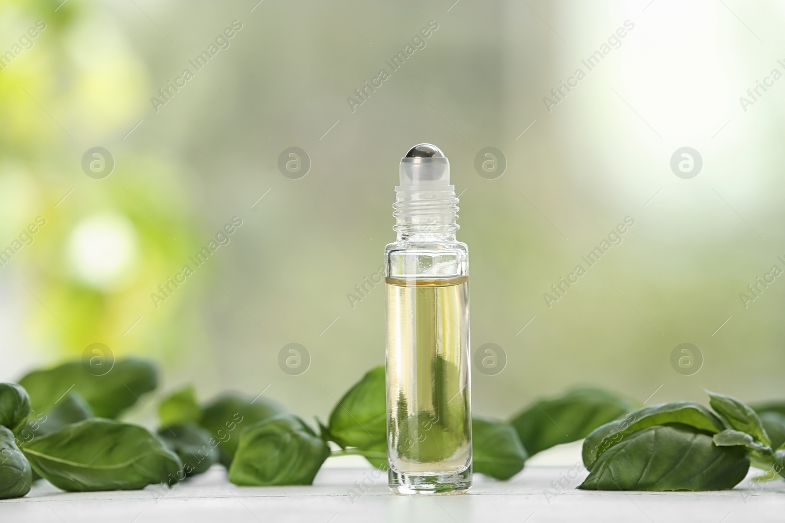 Photo of Bottle of basil essential oil on white wooden table against blurred background