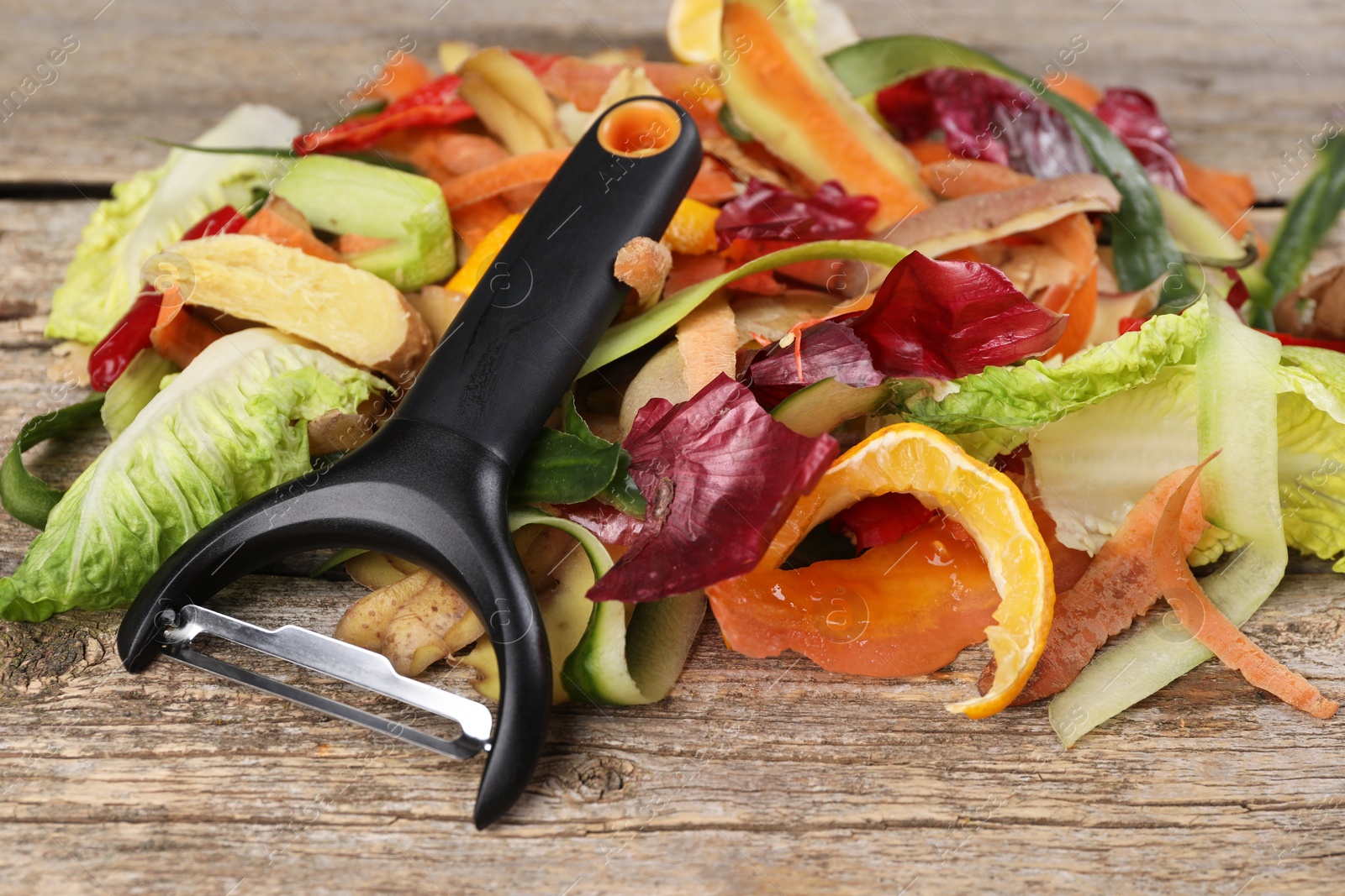 Photo of Peels of fresh vegetables and peeler on wooden table