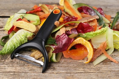 Peels of fresh vegetables and peeler on wooden table