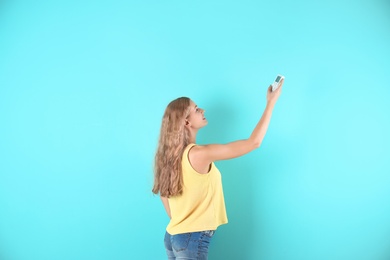 Photo of Young woman with air conditioner remote on color background