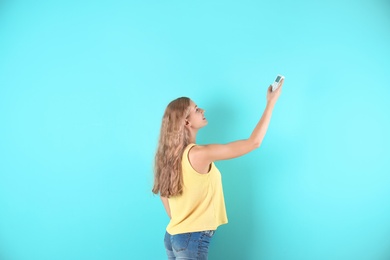 Young woman with air conditioner remote on color background