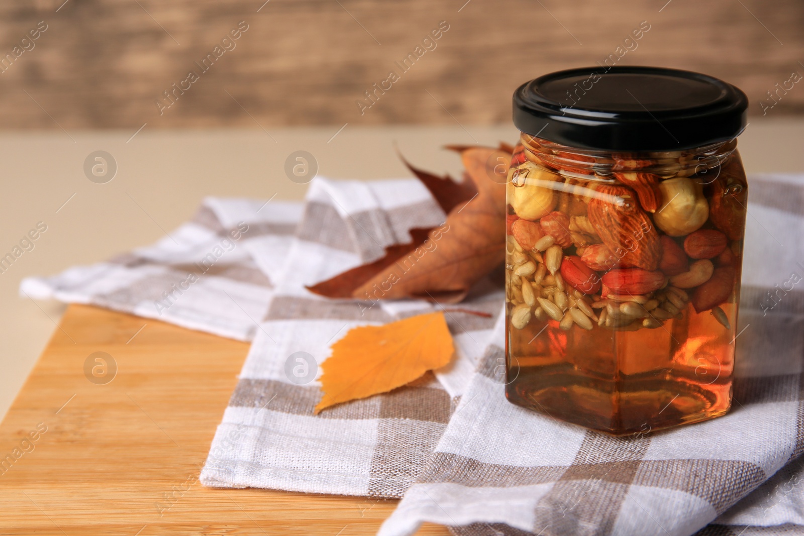 Photo of Different nuts with honey in jar and dry leaves on wooden table. Space for text