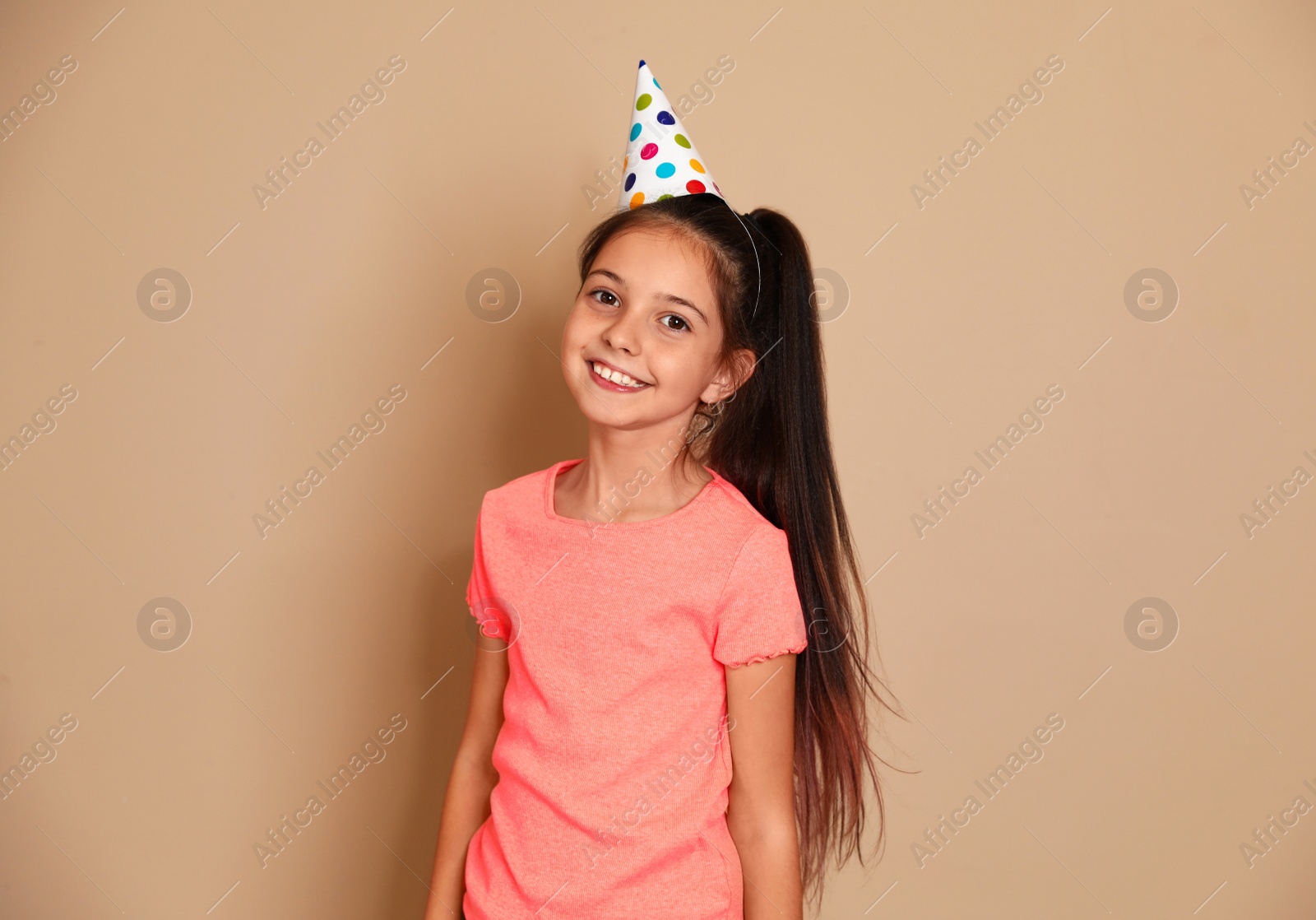 Photo of Happy girl with party hat on brown background. Birthday celebration