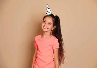 Happy girl with party hat on brown background. Birthday celebration