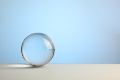 Photo of Transparent glass ball on table against light blue background. Space for text