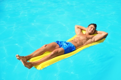 Photo of Young man with inflatable mattress in pool on sunny day