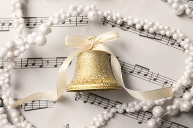 Photo of Golden shiny bell with white bow on music sheets, flat lay. Christmas decoration