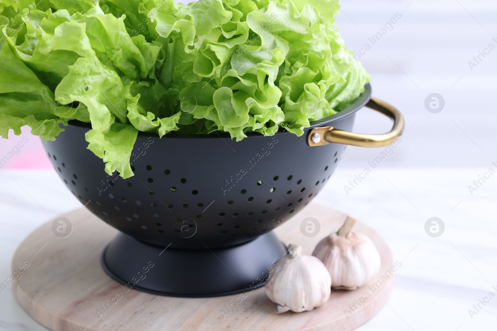 Photo of Fresh lettuce in black colander on white table indoors, closeup