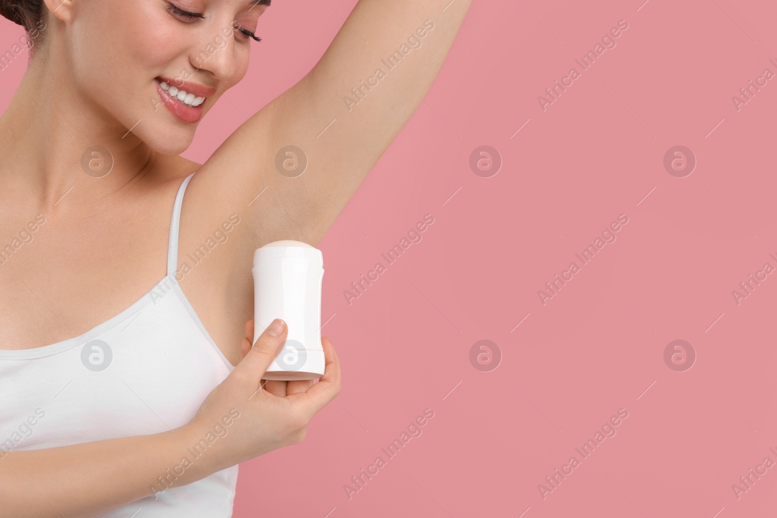 Photo of Beautiful woman applying deodorant on pink background, space for text