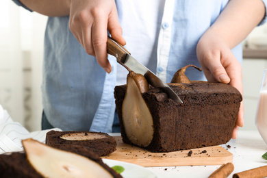 Woman cutting tasty pear bread at table, closeup. Homemade cake