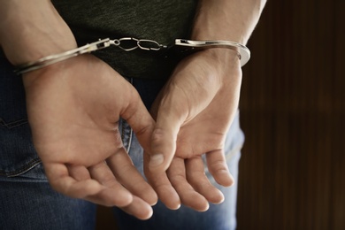 Man detained in handcuffs against blurred wooden background, closeup. Criminal law