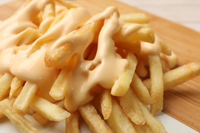 Photo of Delicious french fries with cheese sauce on board, closeup