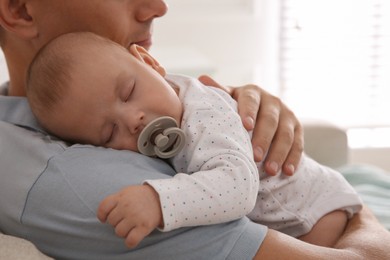 Photo of Father holding his cute sleeping baby with pacifier at home, closeup