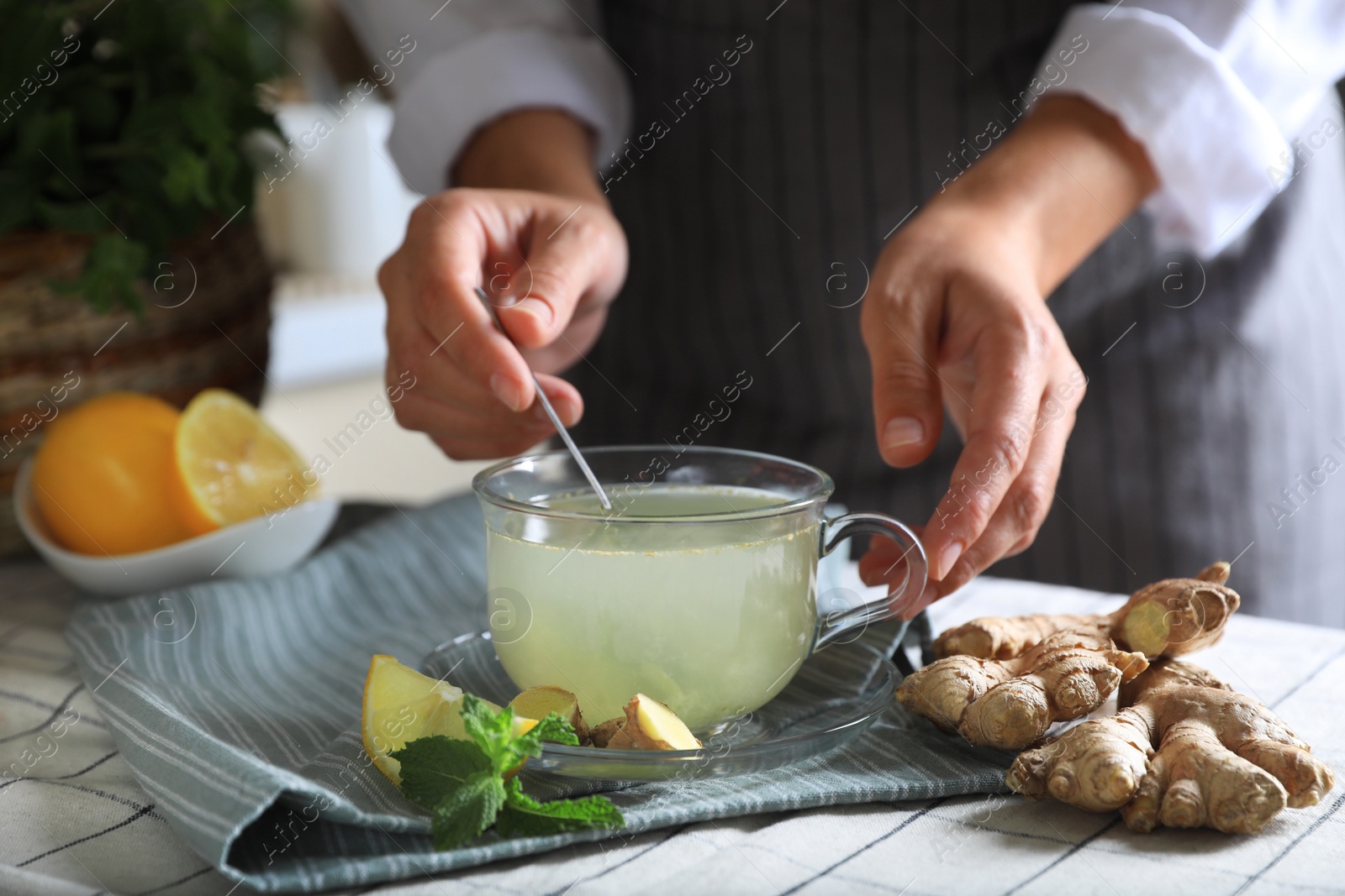 Photo of Woman making aromatic ginger tea at table indoors, closeup