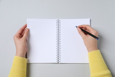 Woman with pen and notepad on light background, top view