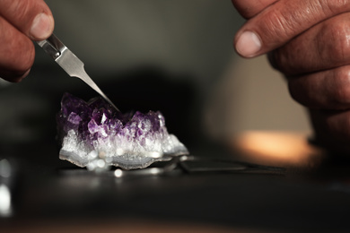 Photo of Professional jeweler working with beautiful amethyst at table, closeup