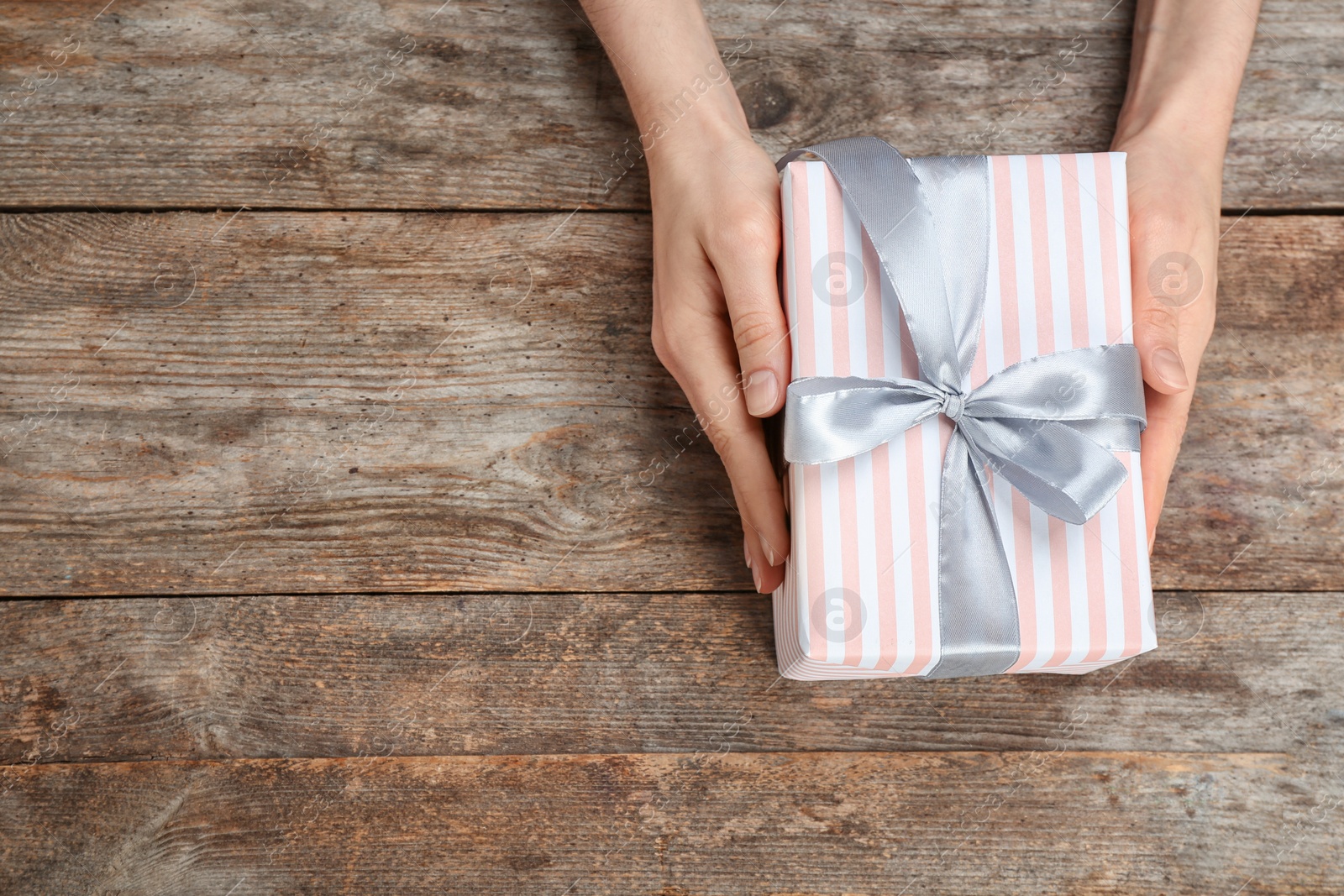 Photo of Young woman holding beautiful gift box on wooden background, top view