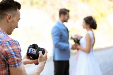 Photo of Professional photographer with camera and wedding couple, outdoors