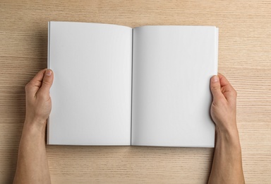 Woman holding brochure with blank pages on wooden background, top view. Mock up for design