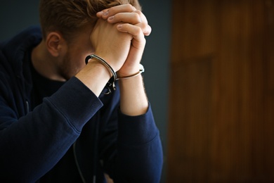 Photo of Man detained in handcuffs indoors, space for text. Criminal law