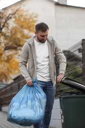 Photo of Man putting garbage bag into recycling bin outdoors