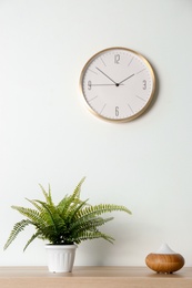 Photo of Modern aroma lamp and houseplant on wooden table near light wall