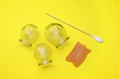 Photo of Glass cups, gua sha and torch on yellow background, flat lay. Cupping therapy